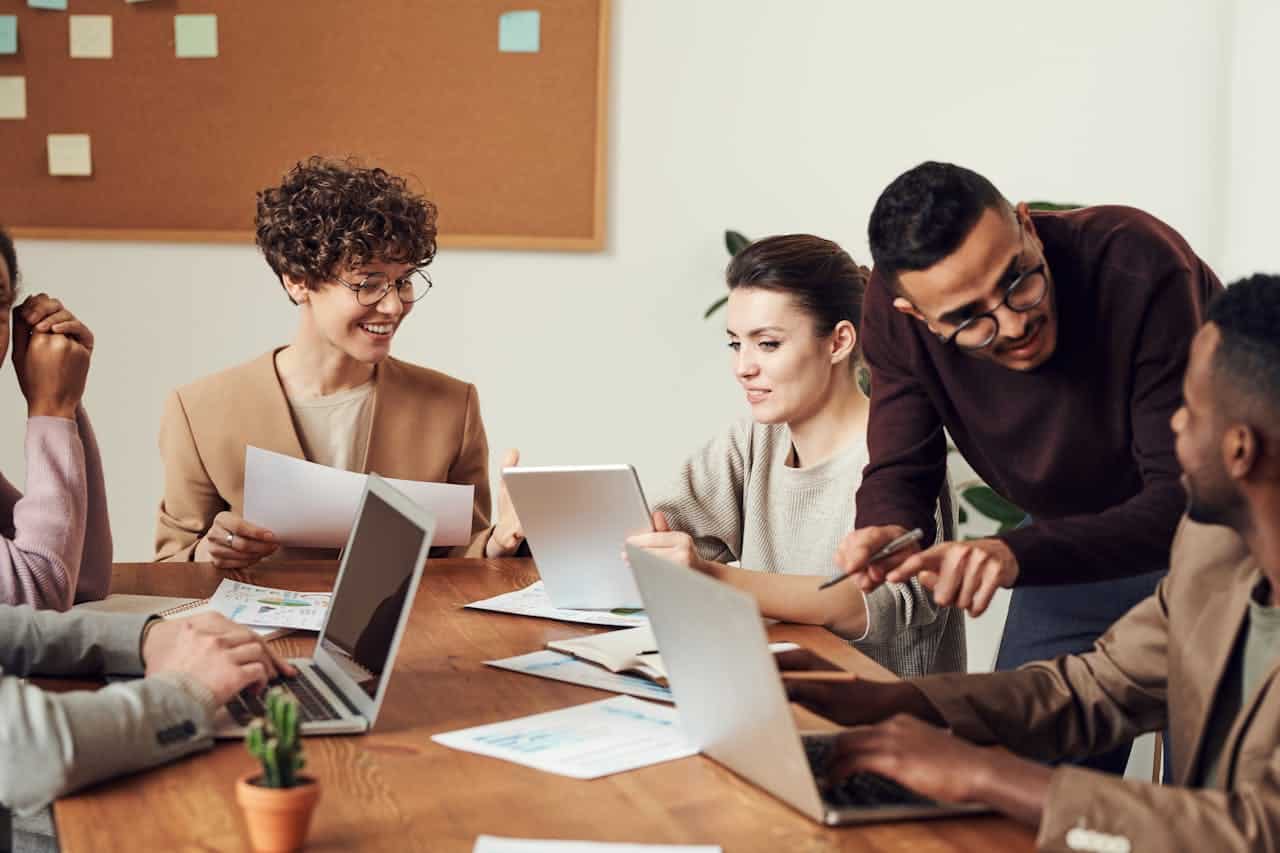 Six people sitting around a conference table. There are laptops and papers on the table.