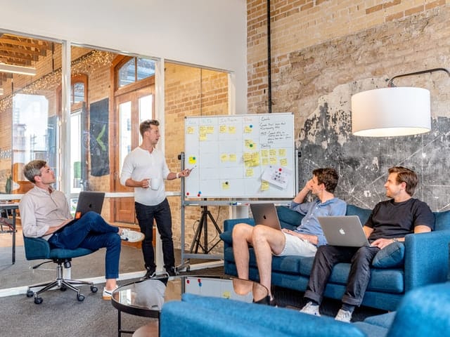 Professionals dressed causally around a white board in a meeting