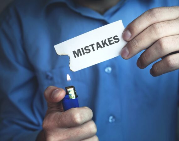 Person holding paper with the word "mistakes" on it and a lighter, as if to get rid of mistakes.