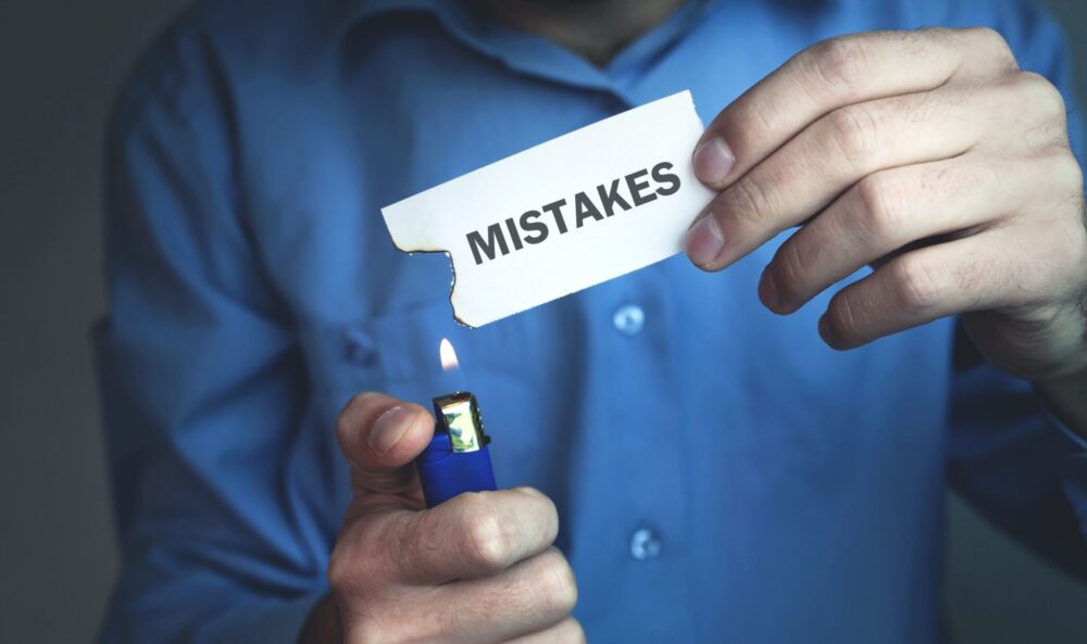 Person holding paper with the word "mistakes" on it and a lighter, as if to get rid of mistakes.