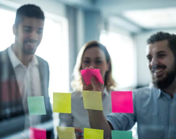 A group of 3 product managers posting sticky notes on a pane of glass.