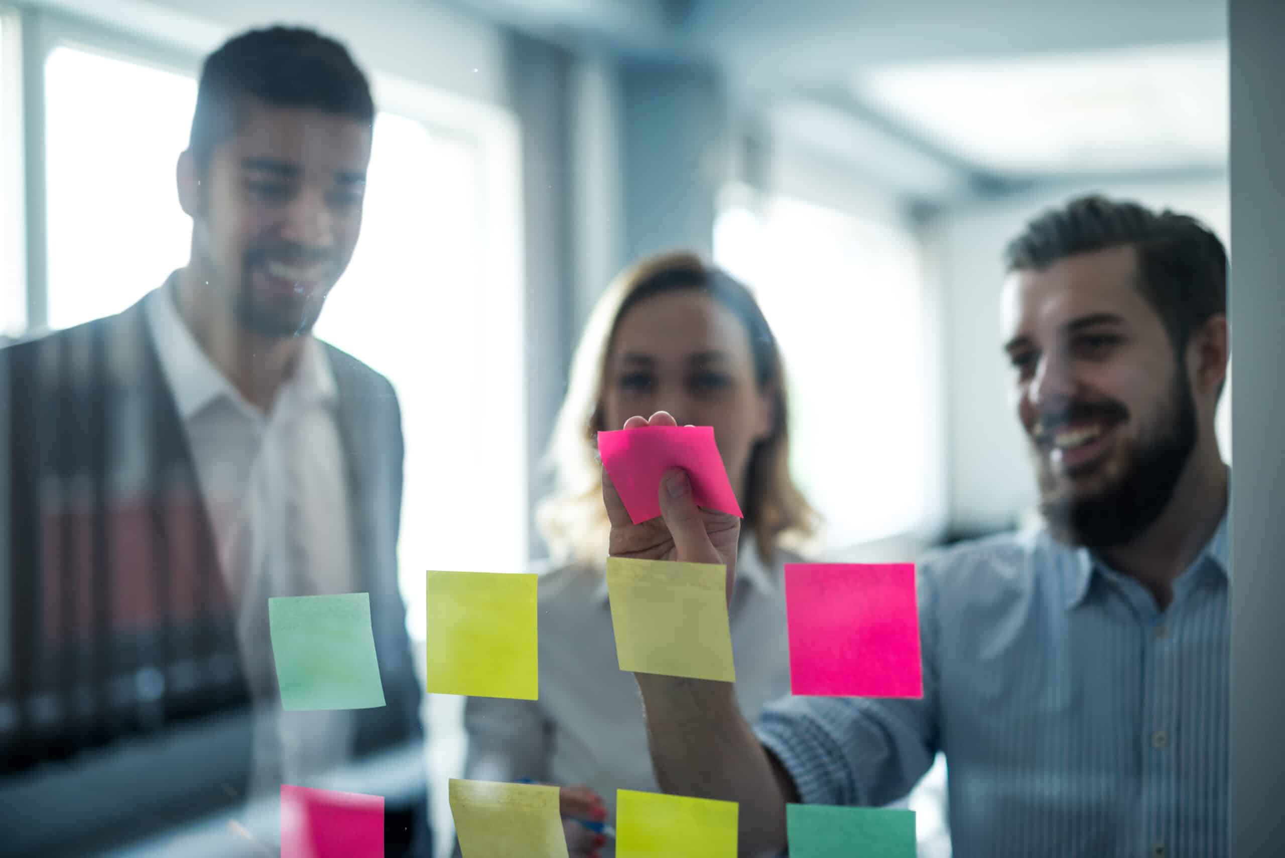 A group of 3 product managers posting sticky notes on a pane of glass.