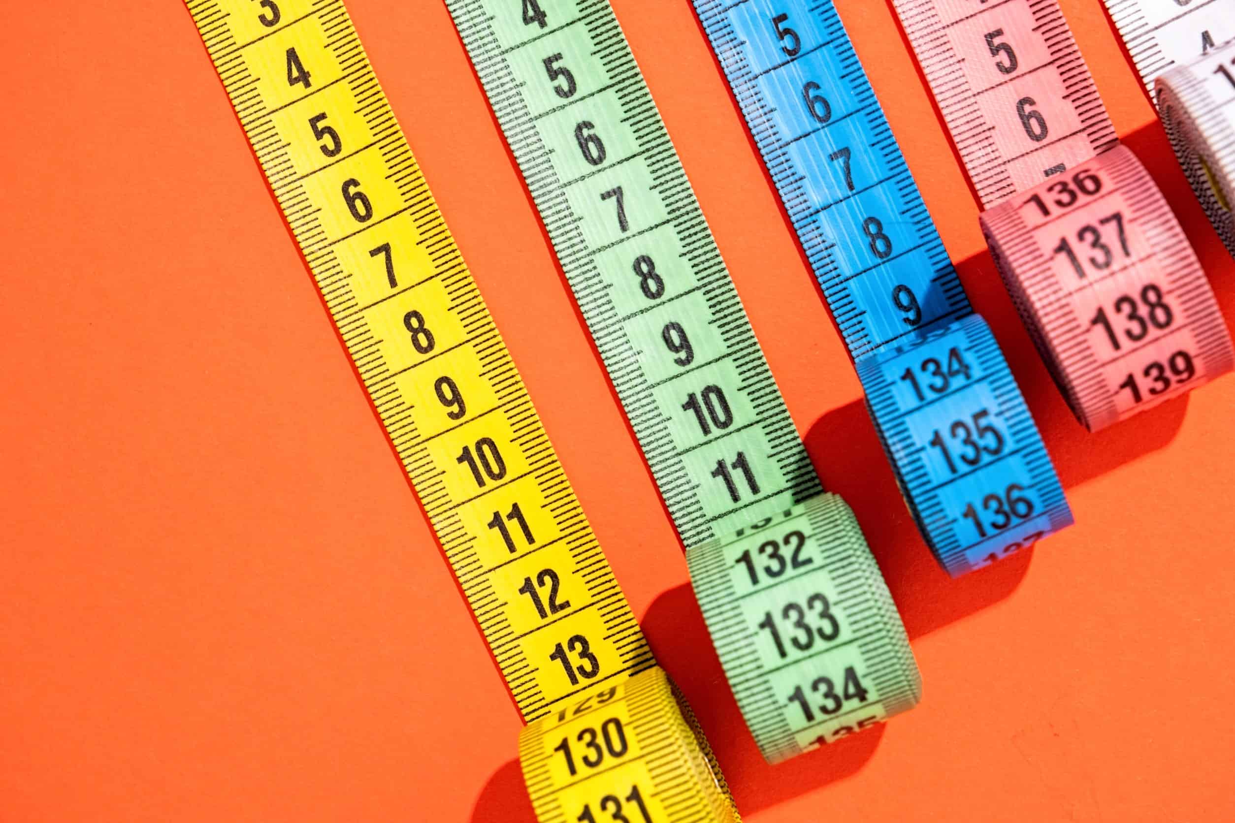 Four measuring tapes against an orange background.