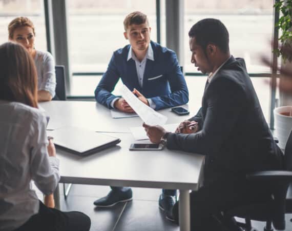 A sales team lead sitting with sales reps at an office table.