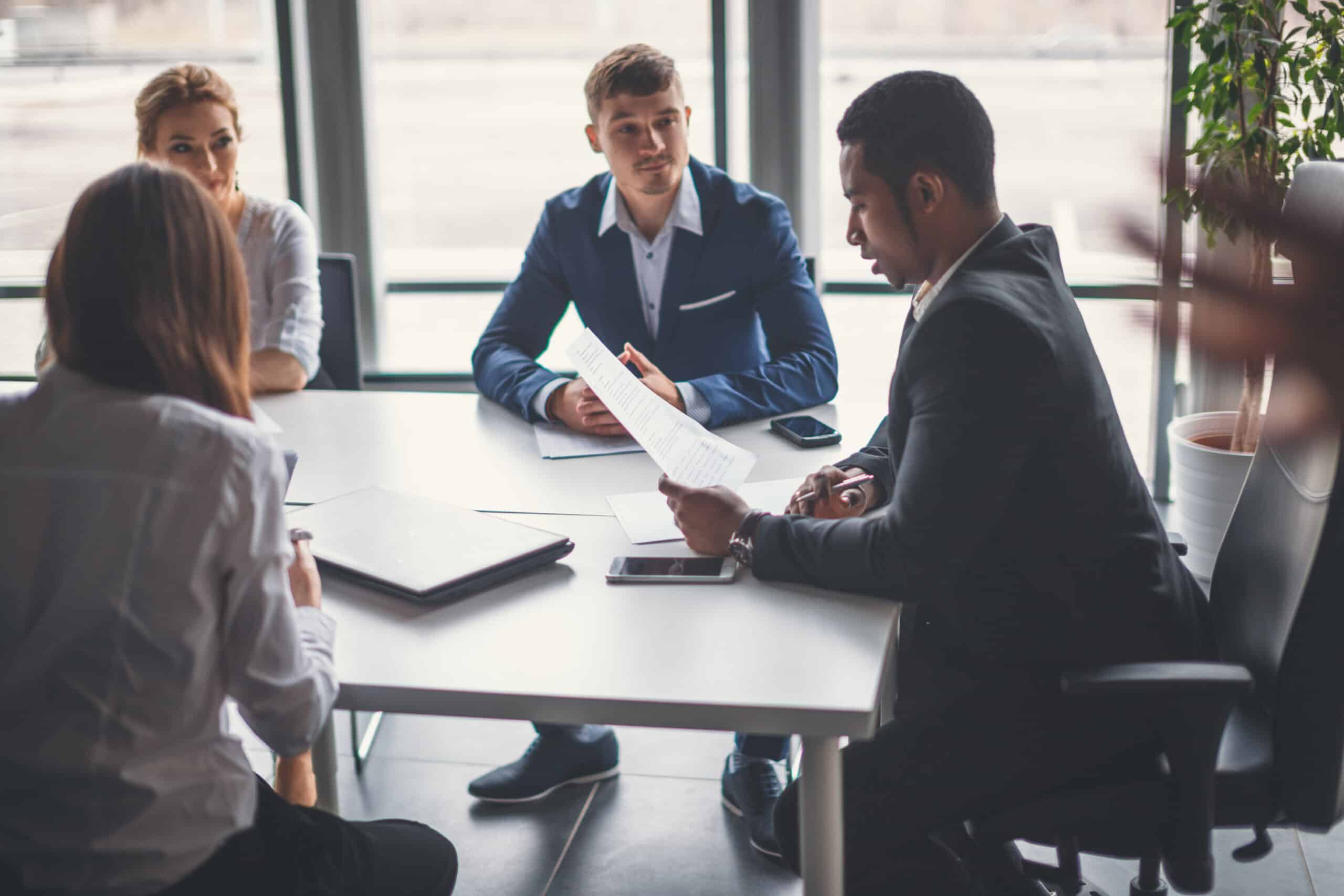 A sales team lead sitting with sales reps at an office table.