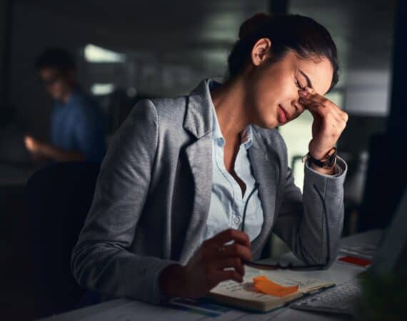 A woman leaning over her laptop, pinching the bridge of her nose in a stressed-out way.