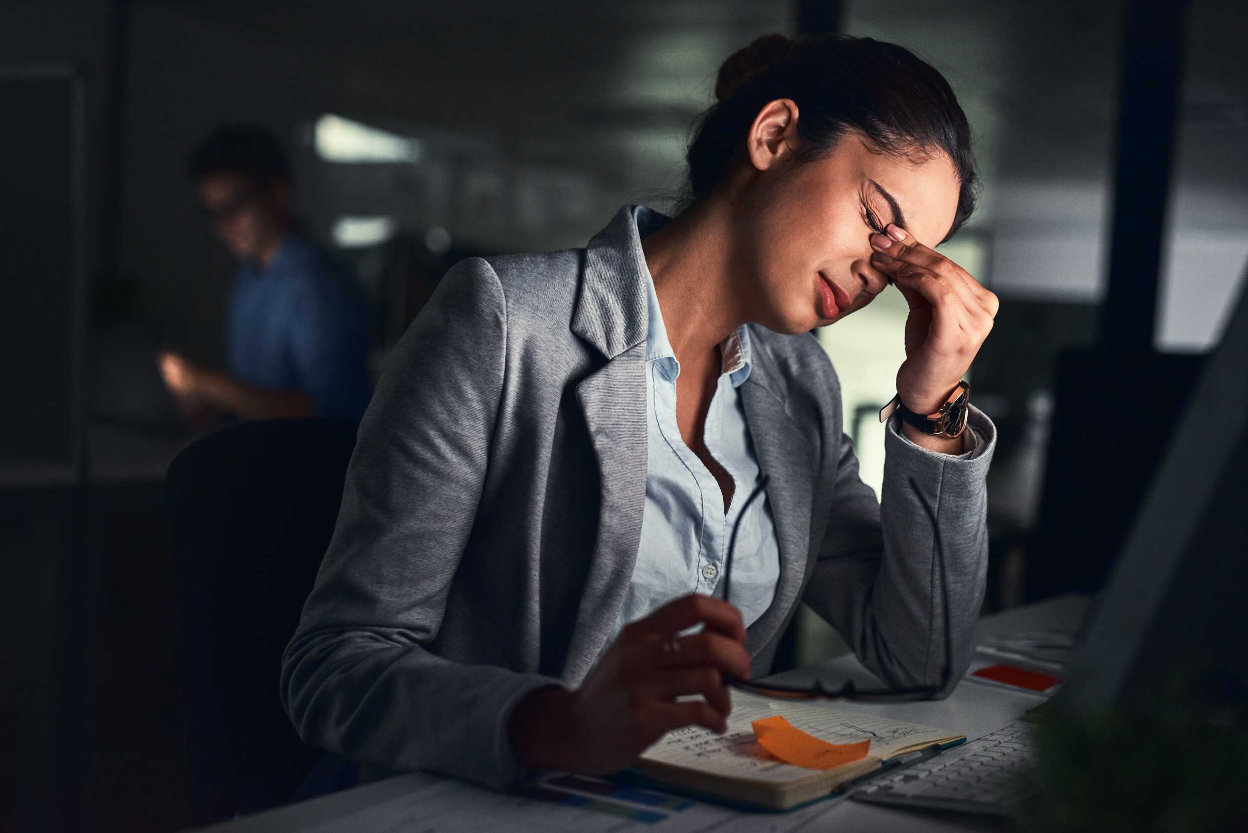 A woman leaning over her laptop, pinching the bridge of her nose in a stressed-out way.