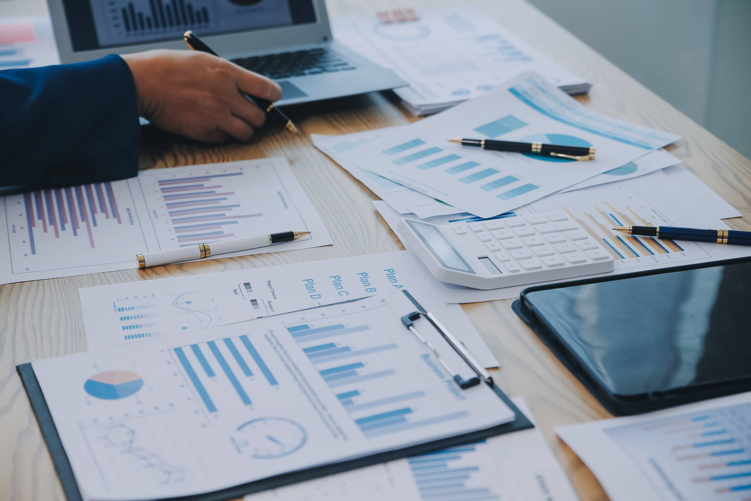 A person sitting at a desk covered with spreadsheets and data visualizations.