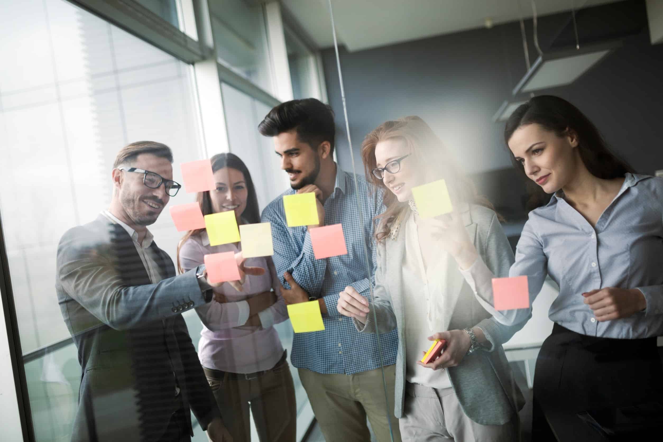 A group of colleagues brainstorming market problems with sticky notes on a clear glass window.