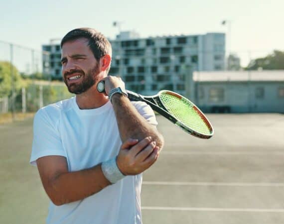 Man holding elbow with tennis racket in hand