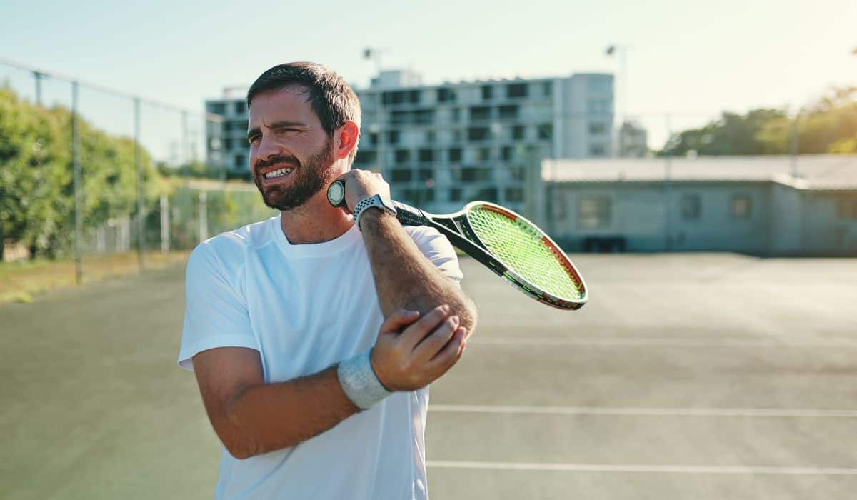 Man holding elbow with tennis racket in hand