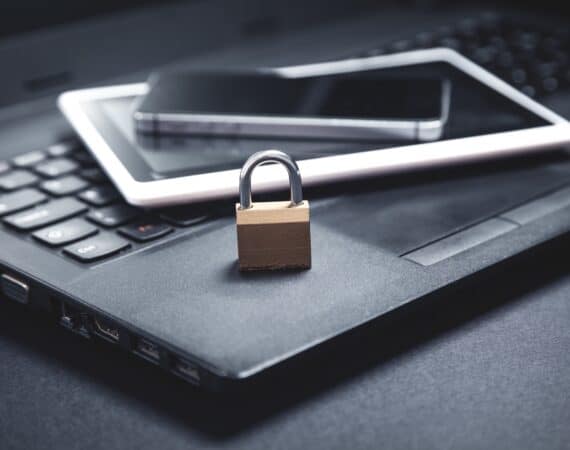 A laptop, tablet, and cell phone stacked on top of each other with a padlock on top to represent data security and data ethics.