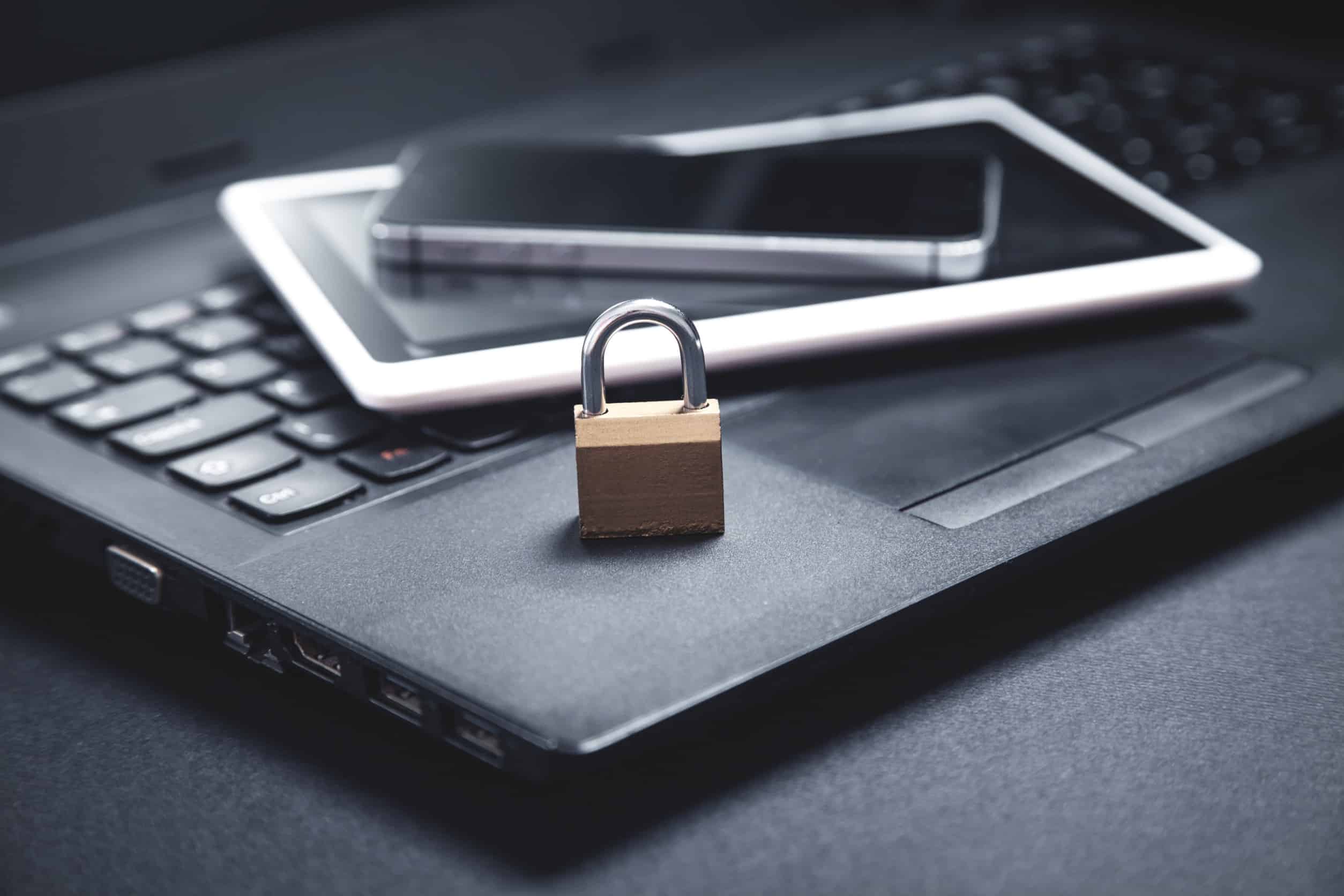 A laptop, tablet, and cell phone stacked on top of each other with a padlock on top to represent data security and data ethics.
