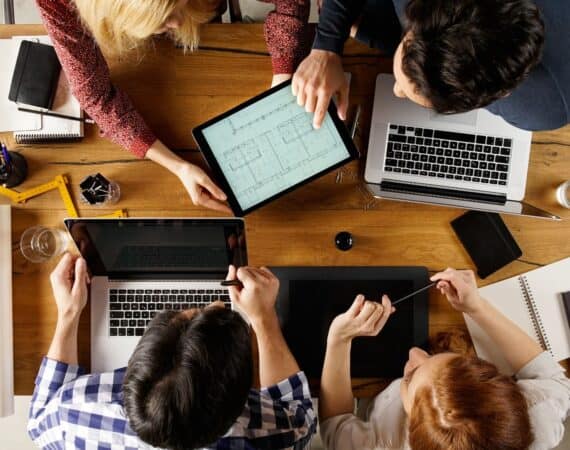 Four people sitting at a table with a tablet and computer working to design solutions for an ambiguous problem