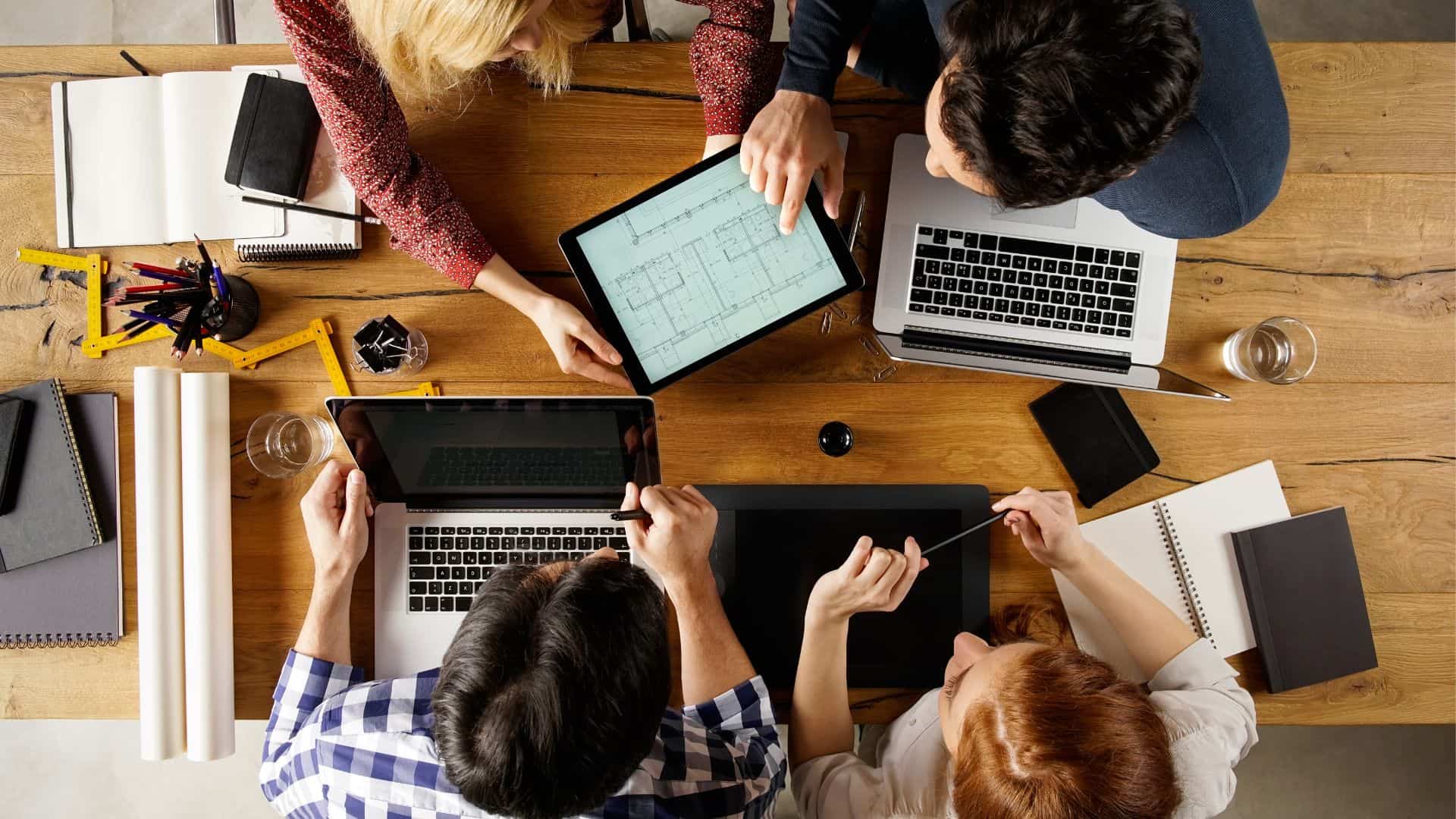 Four people sitting at a table with a tablet and computer working to design solutions for an ambiguous problem