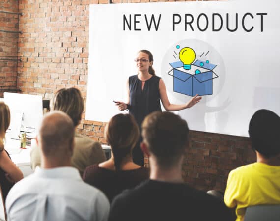 Women In front of group and a board with "New Product" written on it