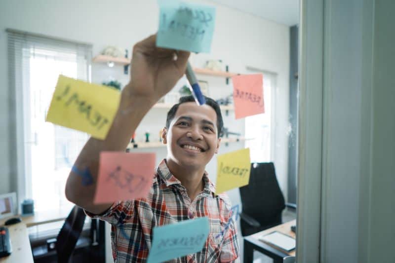 Smiling man in office putting sticky notes on a board
