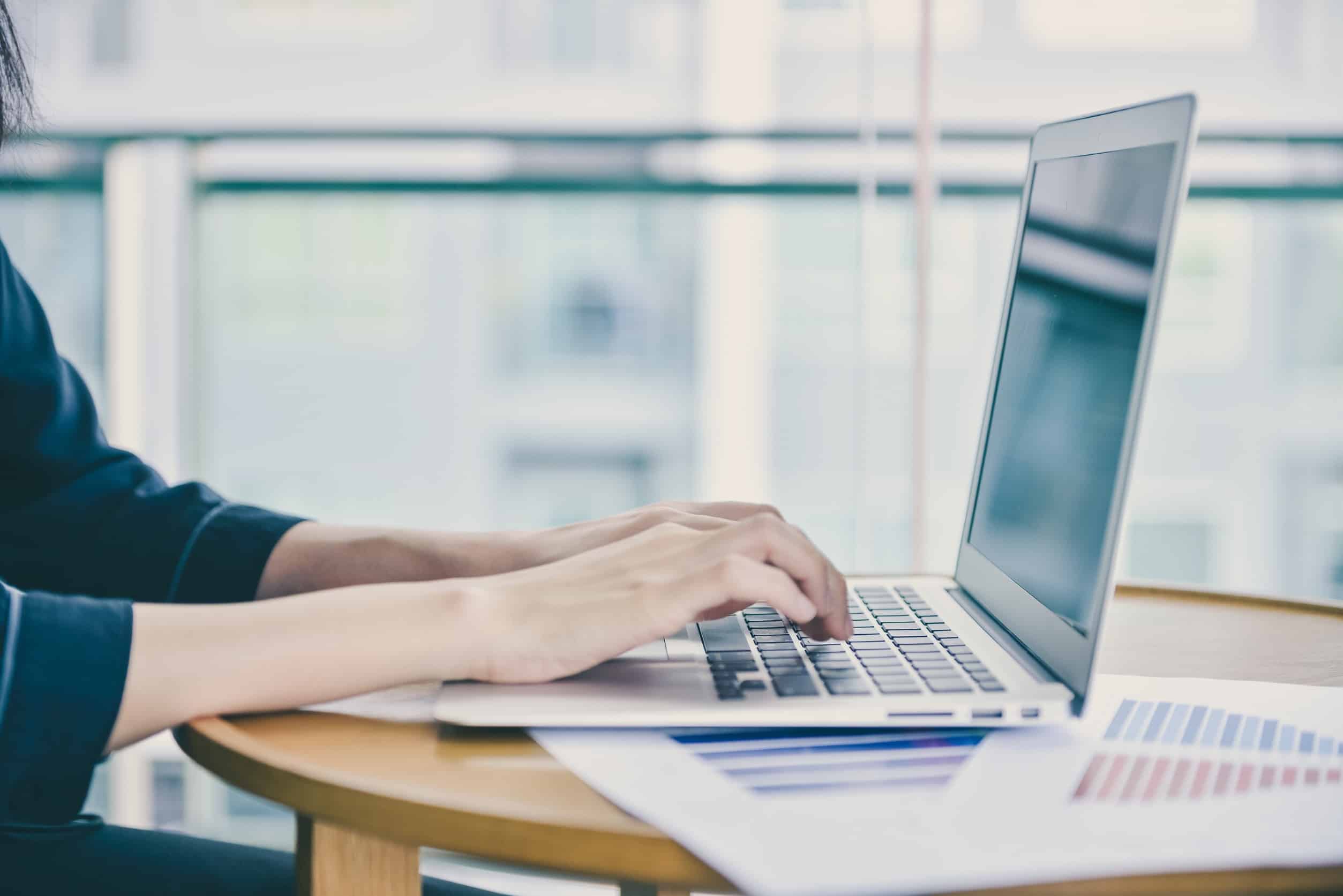 A data scientist working on a laptop, on an office desk surrounded by papers.